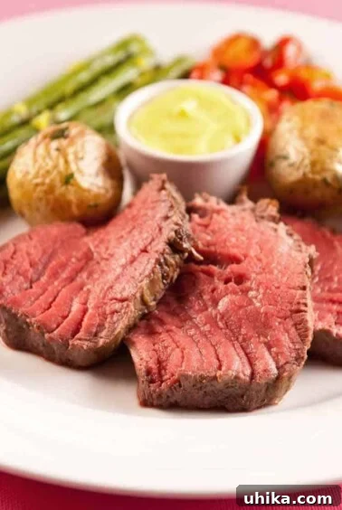 Châteaubriand steak served medium rare, accompanied by Sauce Béarnaise, roasted baby potatoes, roasted asparagus, and cherry tomatoes.