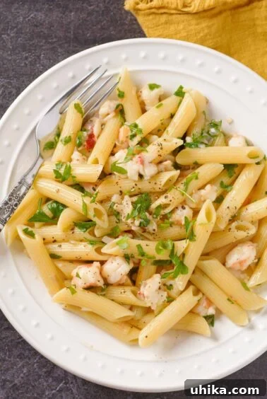 Lobster tail pasta with penne tossed in shallot butter and white wine sauce on a white plate with parsley garnish.