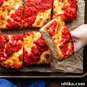Pillowy Detroit Pizza 9 Hands holding slice of Detroit pizza, showcasing the crispy edge.