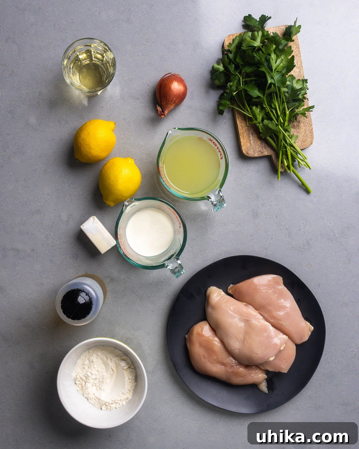 Zesty Lemon Pepper Chicken in Minutes 4 A flat lay photograph showcasing all the fresh ingredients for Creamy Lemon Pepper Chicken: boneless, skinless chicken breasts, fresh lemons, parsley, shallots, butter, heavy cream, olive oil, all-purpose flour, chicken stock, and a bottle of dry white wine.