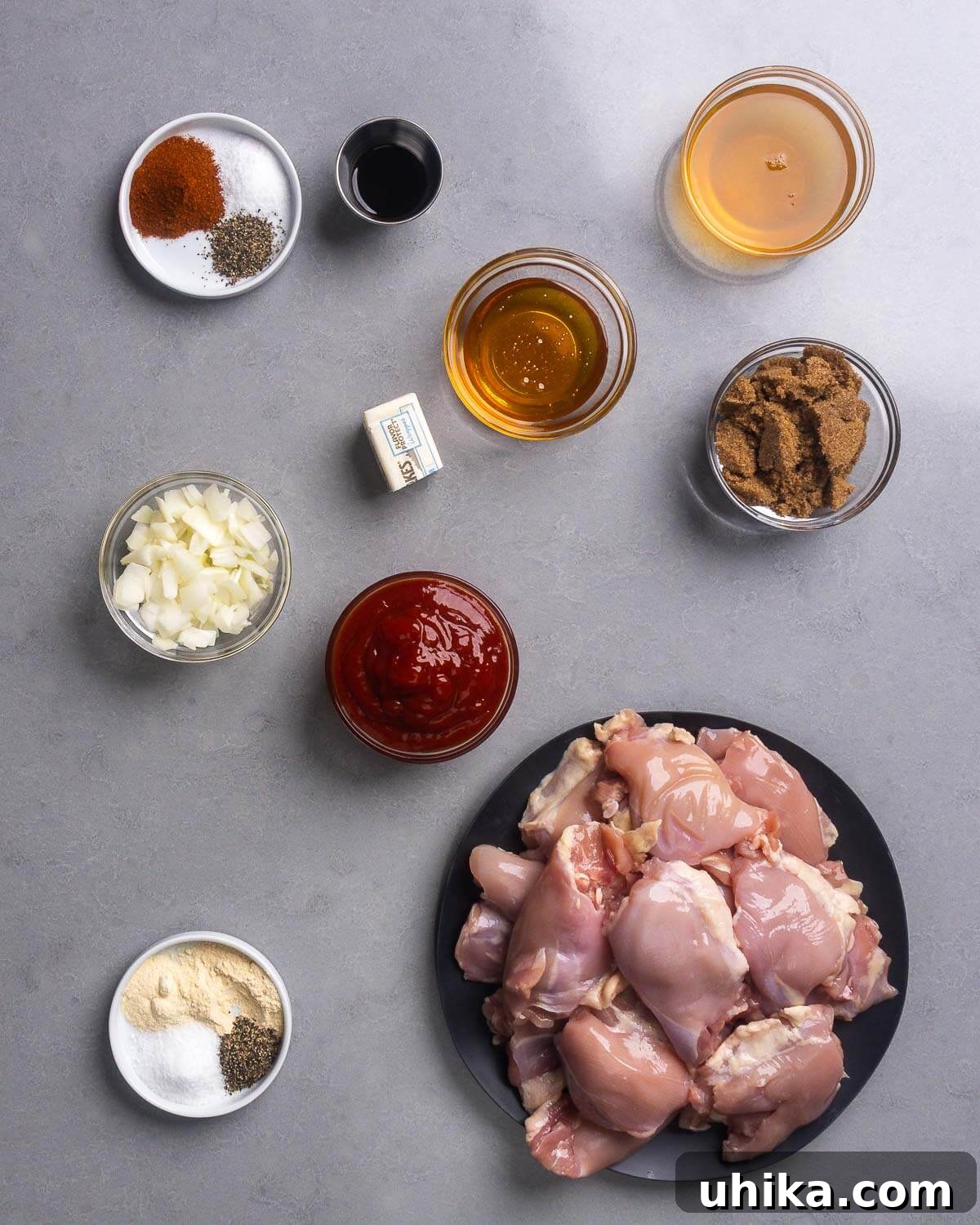 Perfectly Glazed Oven BBQ Chicken Thighs 4 A vibrant flat lay showcasing all the fresh ingredients needed for oven baked bbq chicken thighs: various spices, Worcestershire sauce, butter, honey, apple cider vinegar, dark brown sugar, chopped onion, ketchup, and boneless skinless chicken thighs.