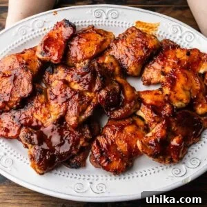 Perfectly Glazed Oven BBQ Chicken Thighs 7 Close-up of hands serving a platter of barbecue chicken thighs, highlighting the glossy sauce and tender meat.