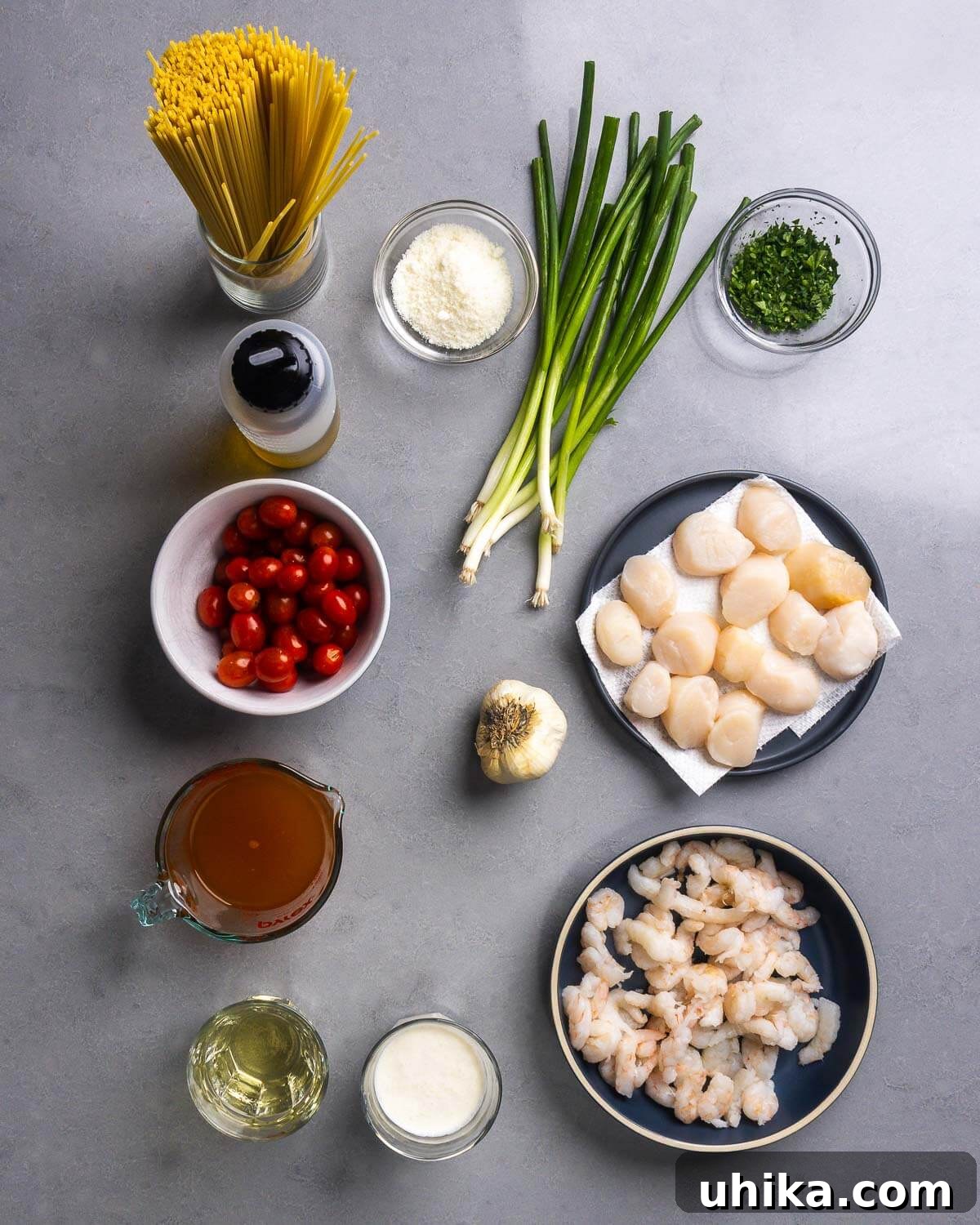 Weeknight Creamy Seafood Pasta 4 Ingredients laid out for creamy seafood pasta: linguine, parmesan cheese, green onions, parsley, olive oil, cherry tomatoes, garlic, scallops, lobster stock, wine, heavy cream, and shrimp.