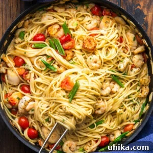 Large black with creamy seafood pasta and kitchen tweezers.