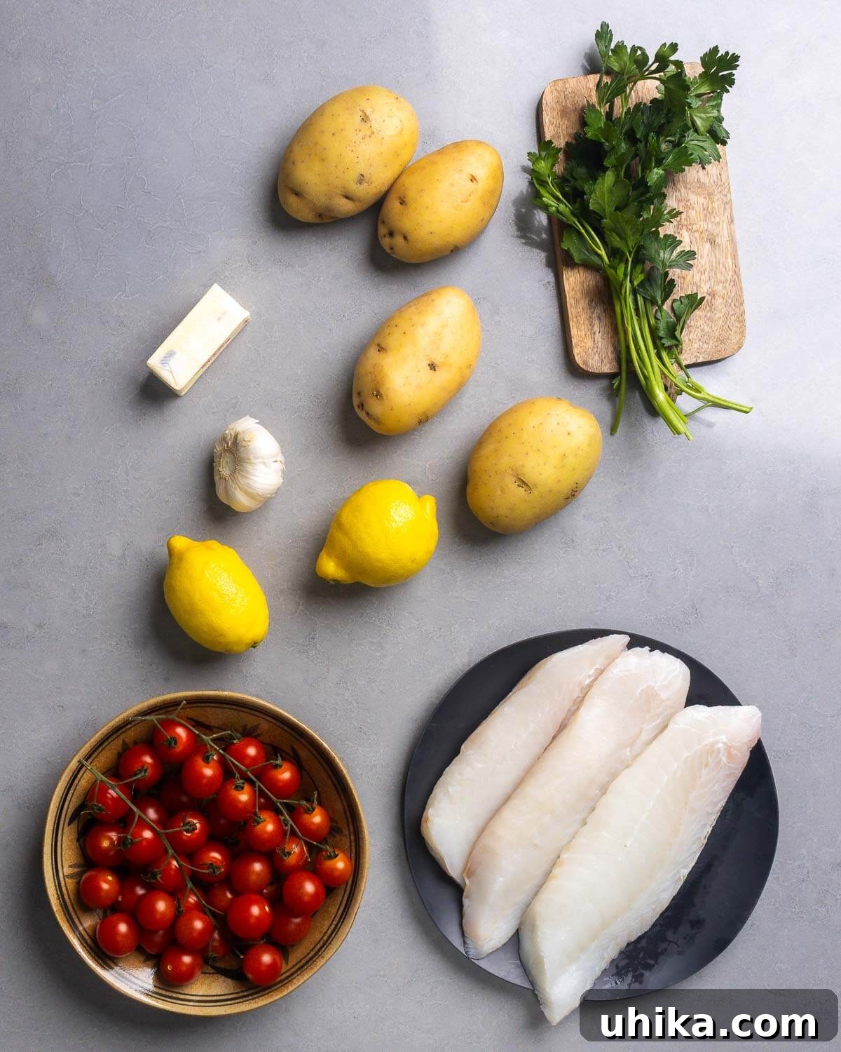 Zesty Lemon Garlic Cod with Golden Potatoes 4 Ingredients shown for baked cod recipe: butter, Yukon gold potatoes, fresh parsley, lemons, juicy cherry tomatoes, and cod fillets.