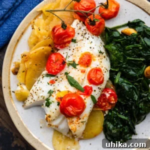 Baked cod with lemon potatoes and cherry tomatoes on white plate, garnished with parsley.