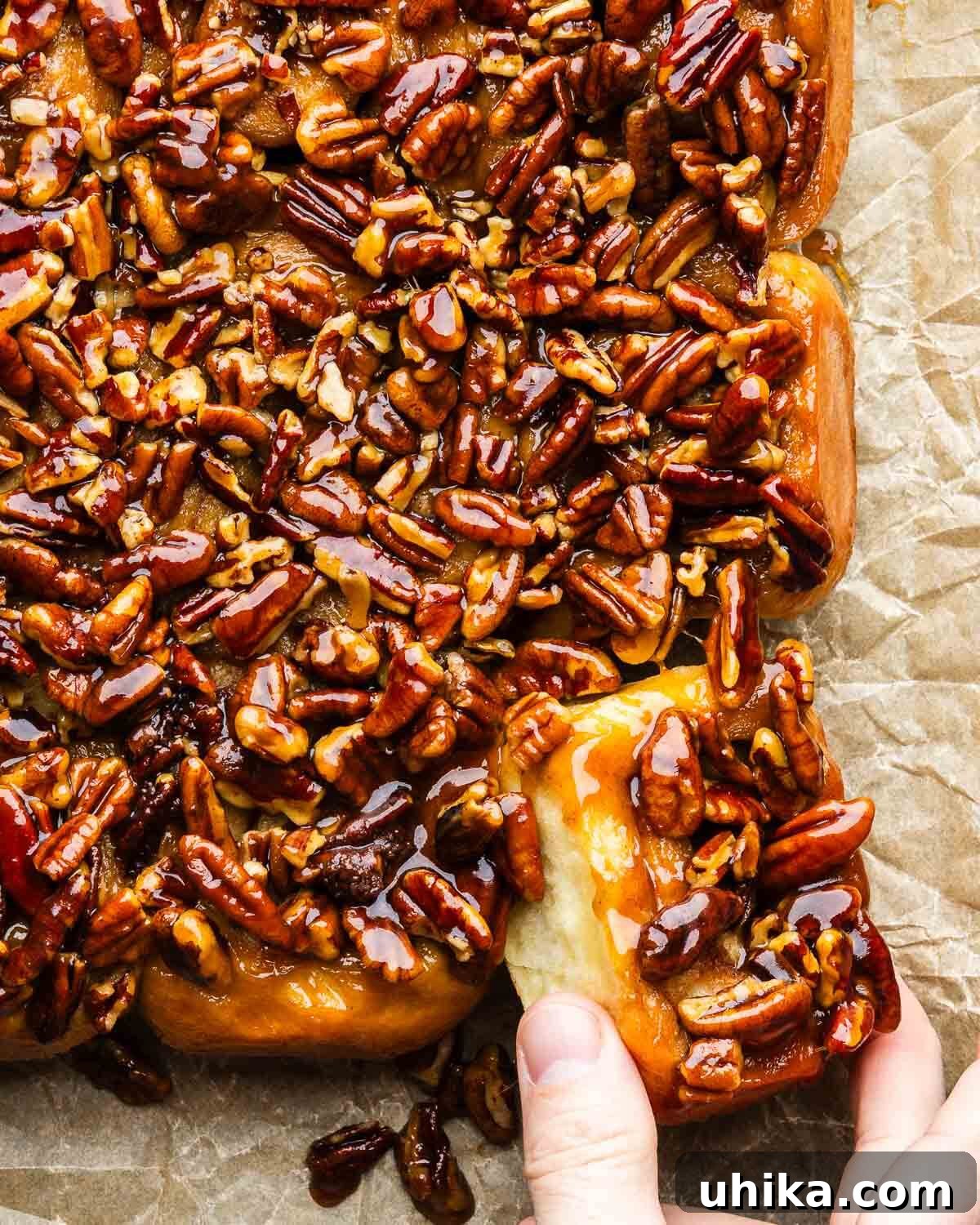 Caramel-Drenched Homemade Sticky Buns 2 Fingers pulling a sticky bun from bunch of buns, highlighting its gooey texture and pecan topping.