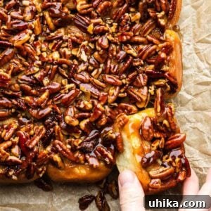 Hands grabbing a sticky bun, showcasing its rich caramel and pecan topping.