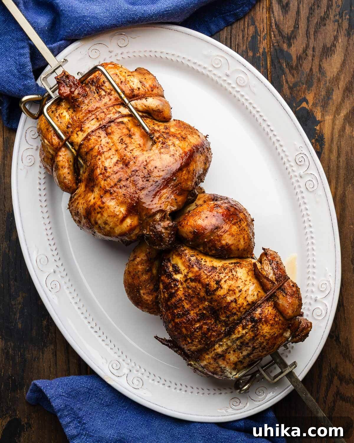 How to Make Authentic Rotisserie-Style Chicken at Home 2 Two rotisserie chickens on only fire weber attachement rod on white platter.