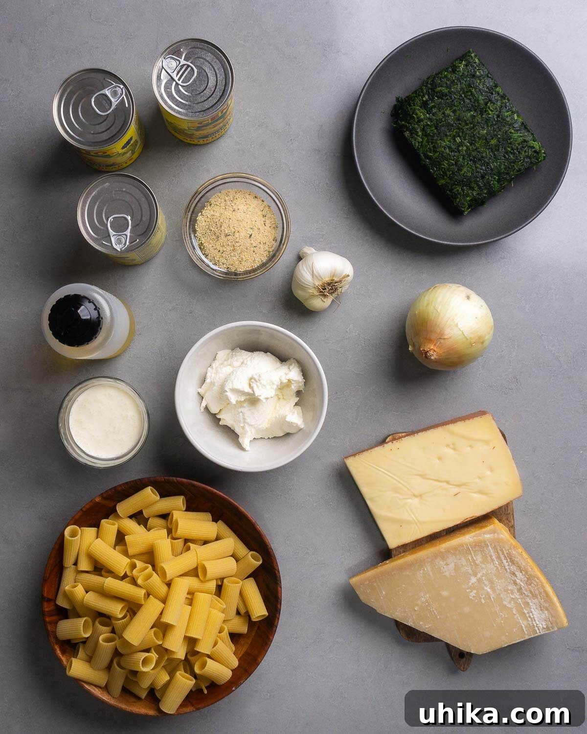 Creamy Baked Spinach and Artichoke Pasta Casserole 4 Ingredients shown: artichoke hearts, breadcrumbs, garlic, spinach, olive oil, heavy cream, ricotta, onion, rigatoni, fontina and parmesan cheese.