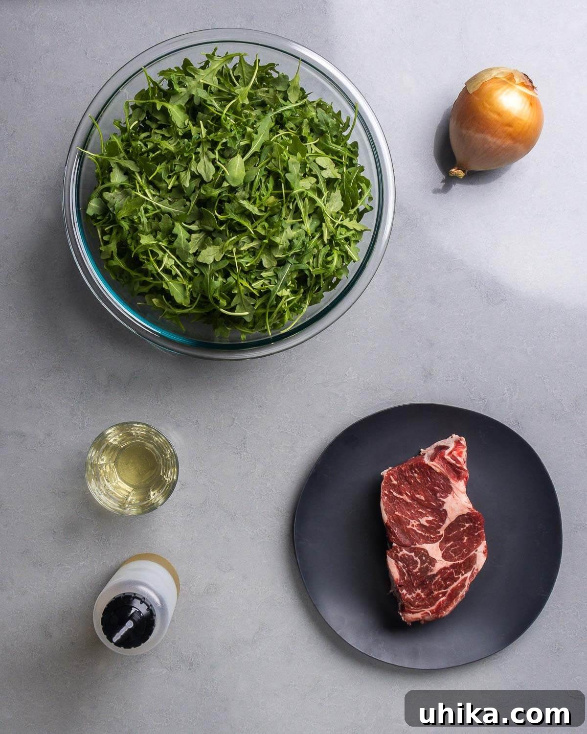 Roman-Style Beef with Peppery Arugula 4 Ingredients shown: baby arugula, onion, white wine, olive oil, and ribeye steak.