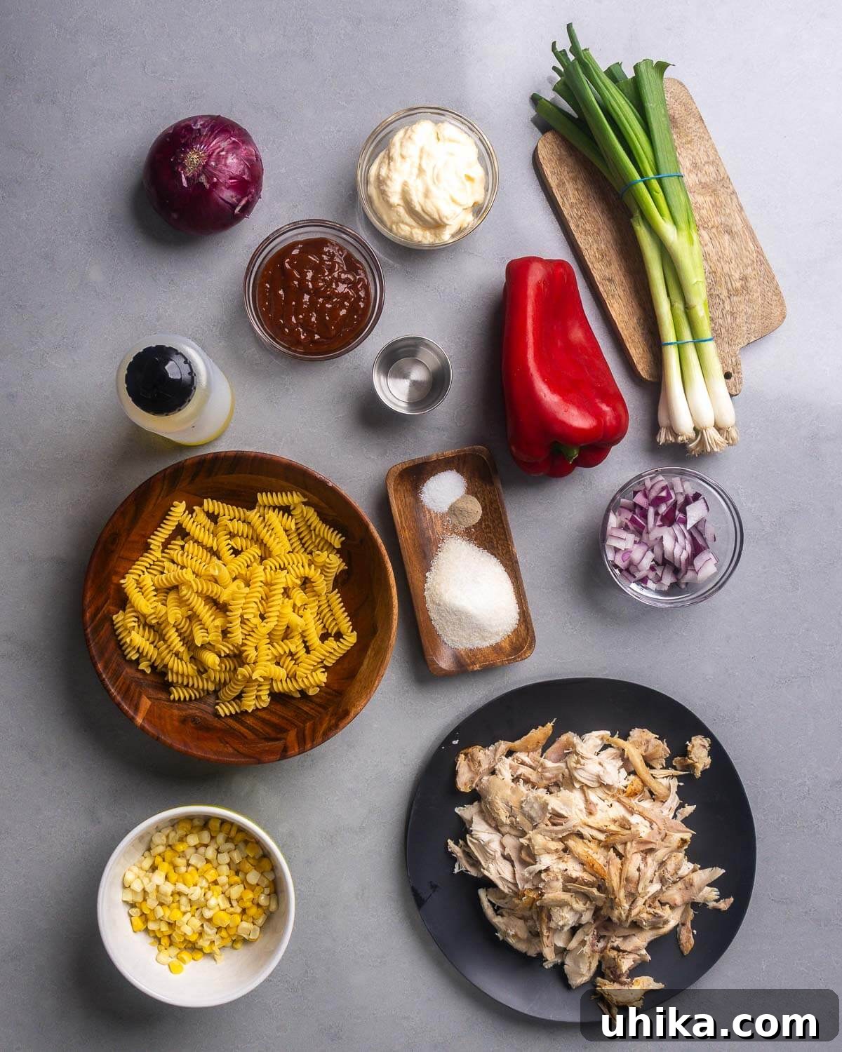 Sweet and Tangy BBQ Chicken Pasta Salad Recipe 4 Ingredients shown: red onion, mayo, bbq sauce, vinegar, green onions, bell pepper, oil, pasta, spices, corn, and broken down rotisserie chicken.