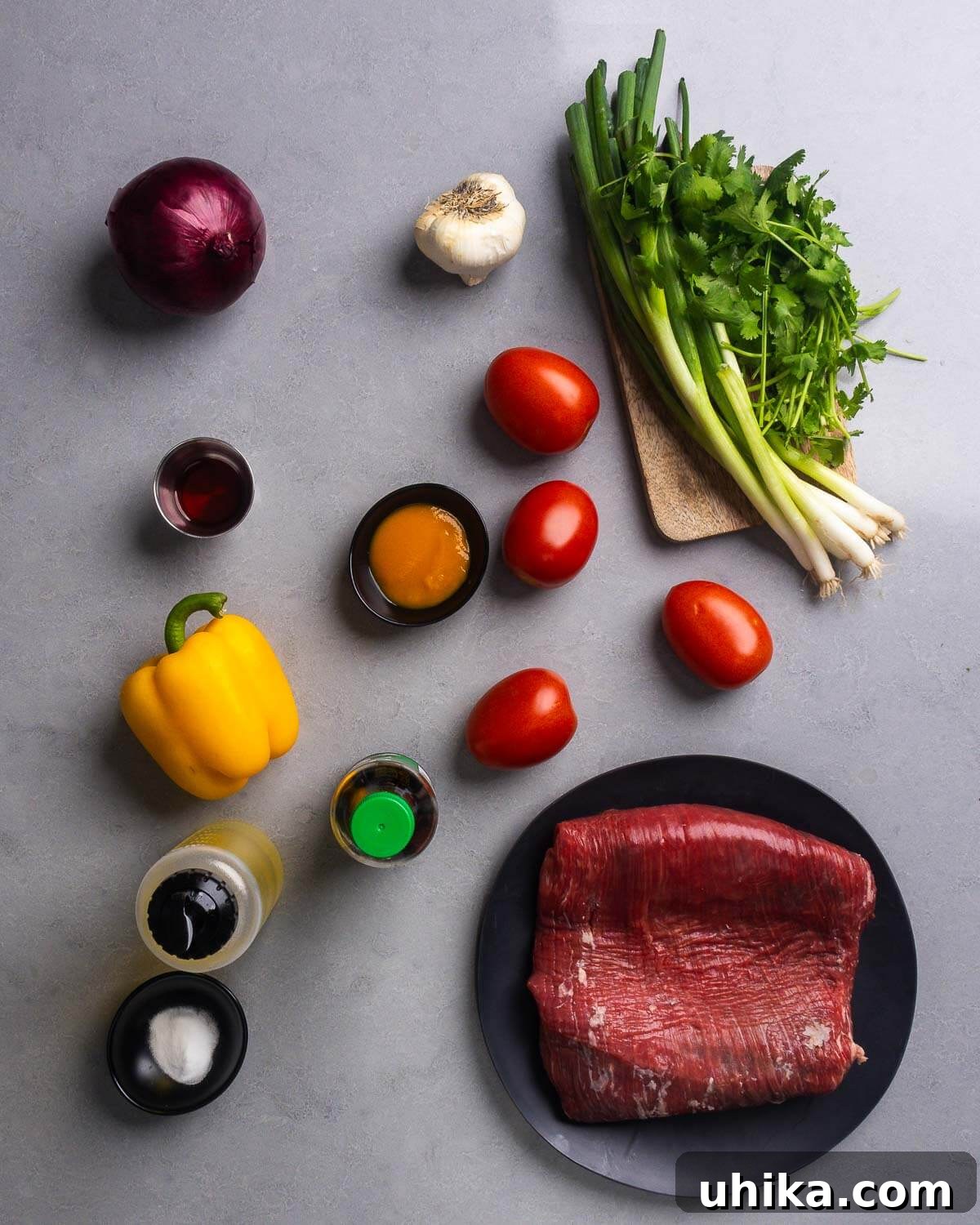 Lomo Saltado: Classic Peruvian Beef Stir-Fry Recipe 4 Ingredients shown: red onion, garlic, green onion, cilantro, red wine vinegar, aji amarillo paste, plum tomatoes, bell pepper, soy sauce, neutral oil, baking soda, and flank steak.
