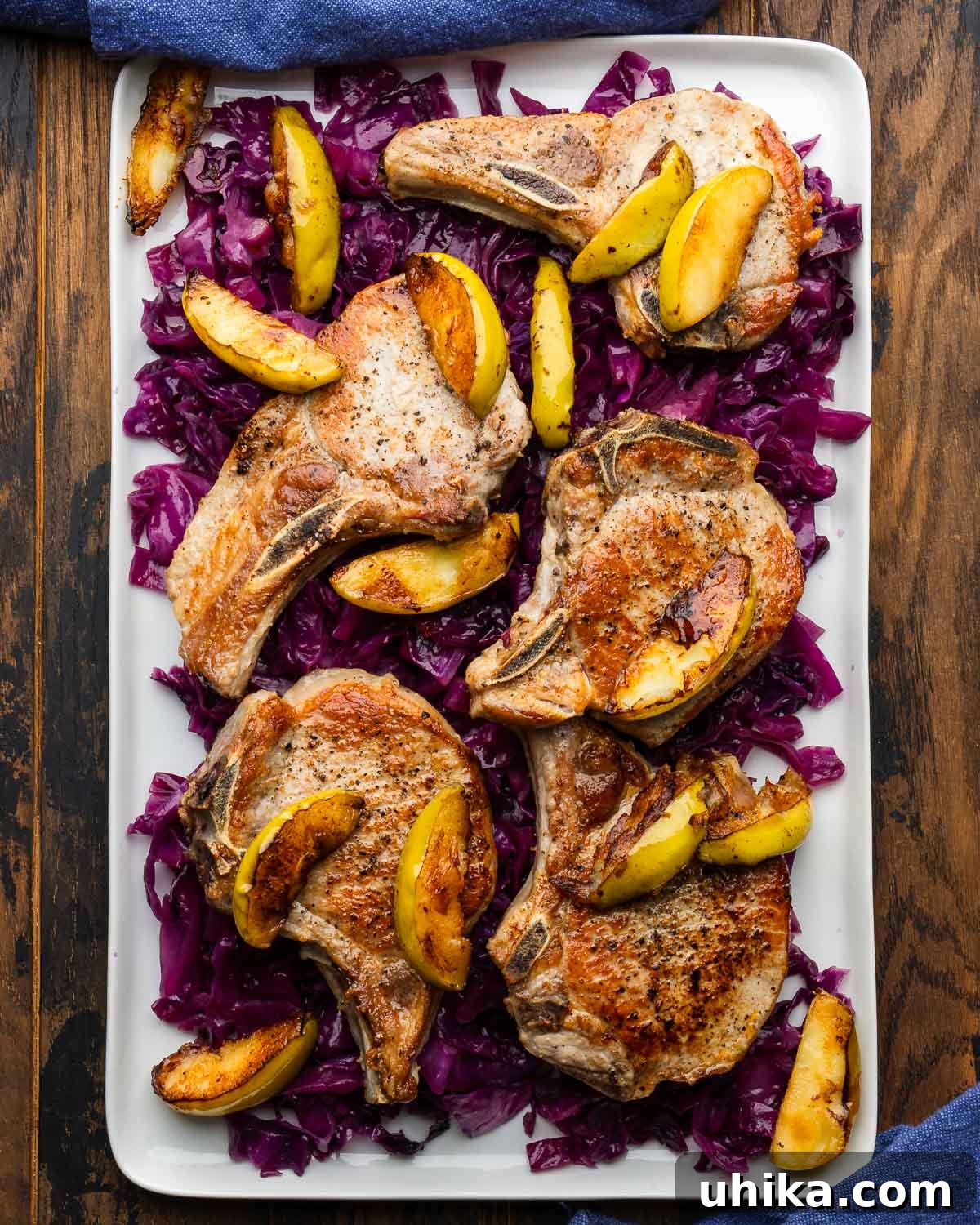 Pan-Seared Pork Chops with Braised Cabbage for Fall 2 Large white platter braised cabbage topped with seared pork chops and apples.