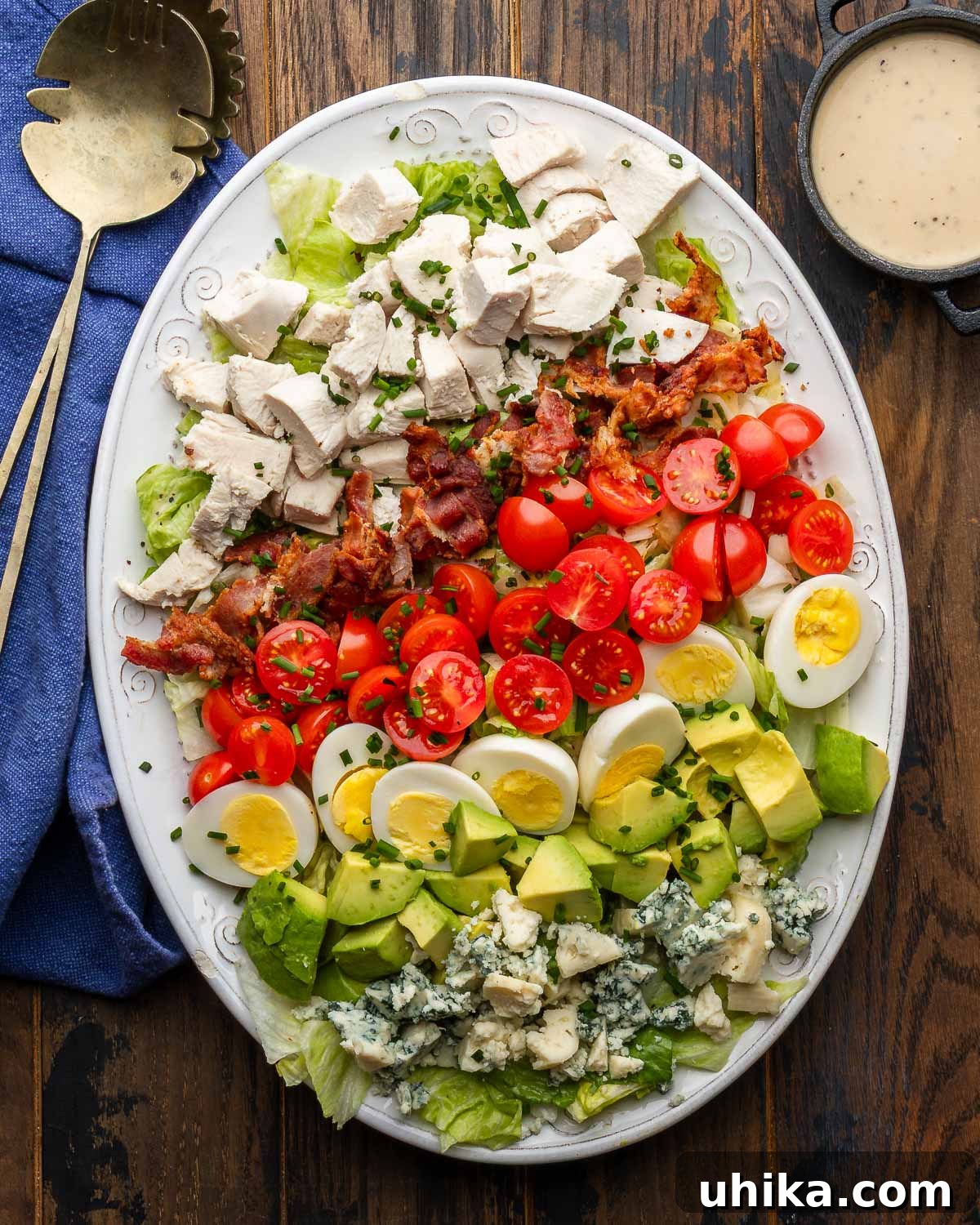 Hearty Cobb Salad Recipe with Avocado and Bacon 2 Cobb salad on white platter with spoons and extra dressing on the side.