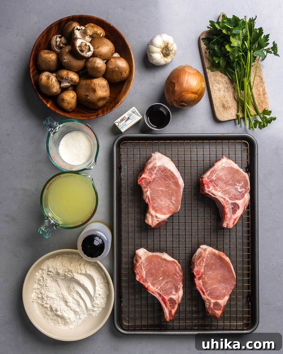 Smothered Pork Chops in Creamy Mushroom Sauce 4 Ingredients shown: mushrooms, garlic, butter, worcestershire sauce, onion, parsley, cream, chicken stock, olive oil, flour, and pork chops.