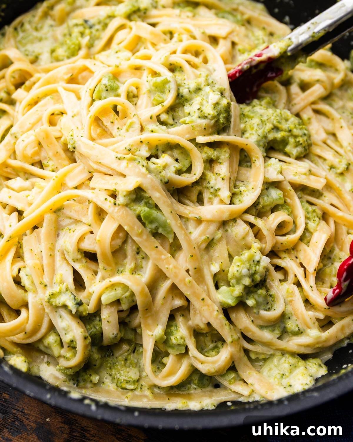 Tongs grabbing broccoli alfredo.